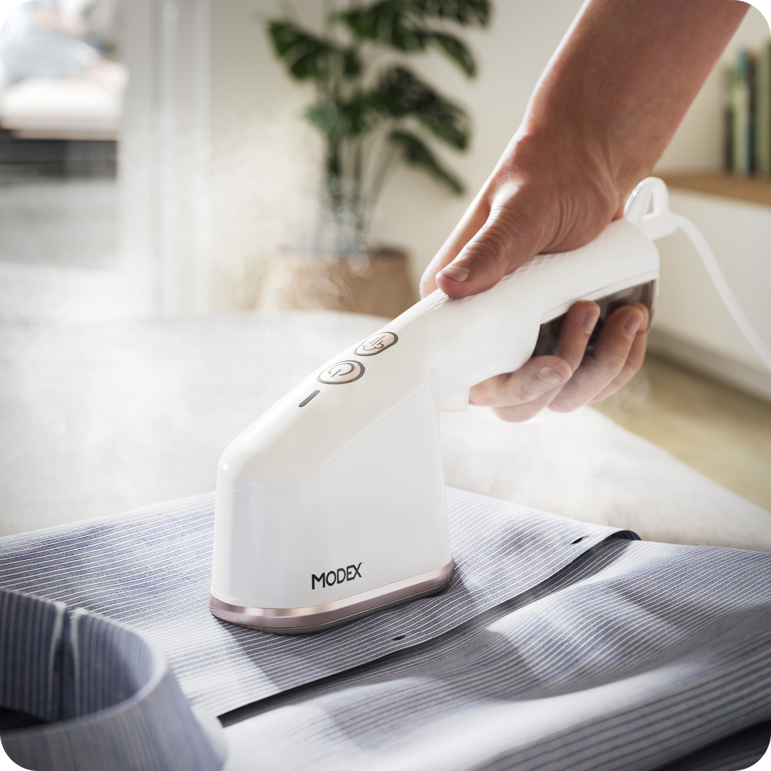 Handheld garment steamer being used horizontally on a striped shirt laid flat.